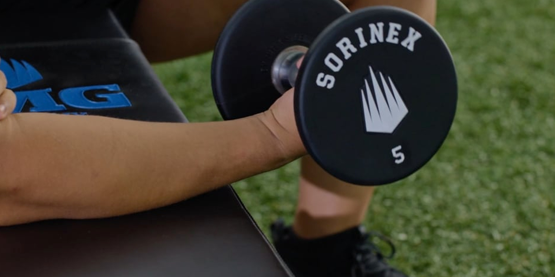 A close view shows a hand holding a dumbbell during a wrist exercise.