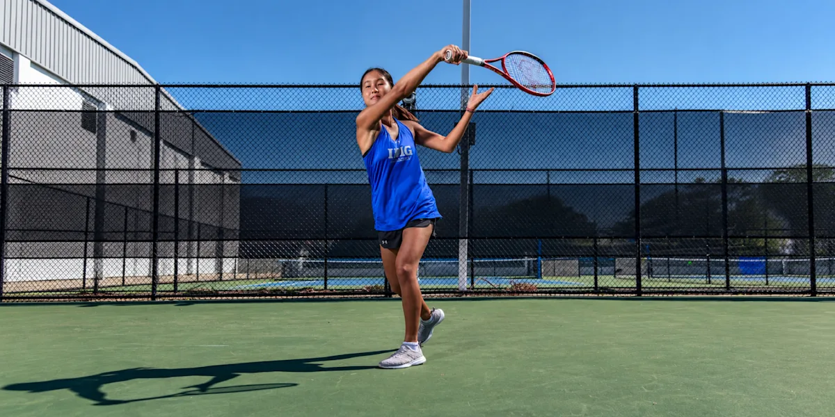 A tennis player swings a racket on an outdoor court.