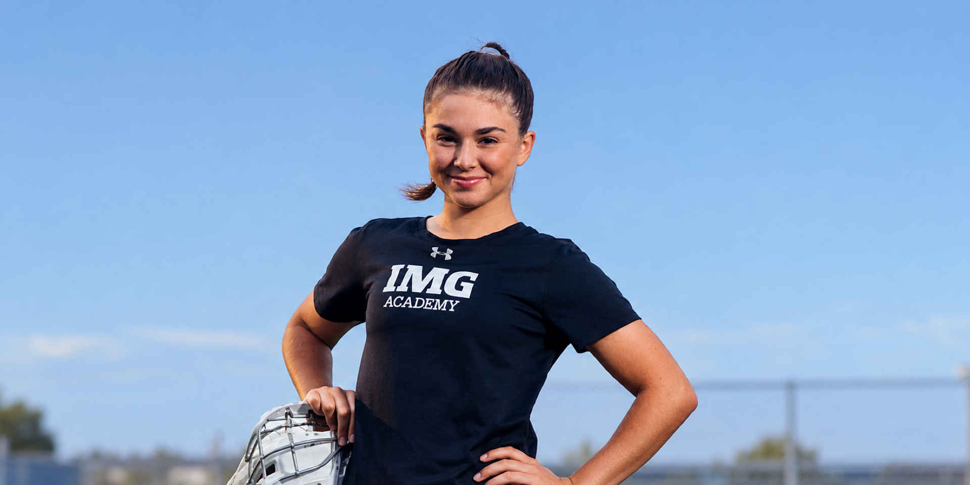 An athlete stands with her hands on her hips against a blue sky.