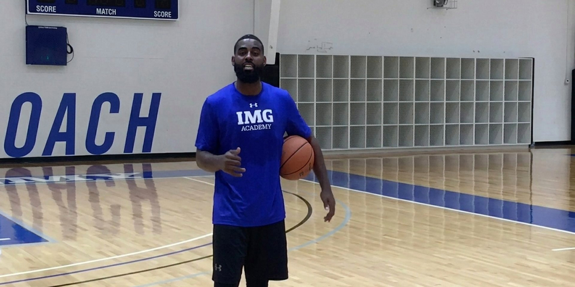A basketball coach speaks while holding a ball on an indoor court.