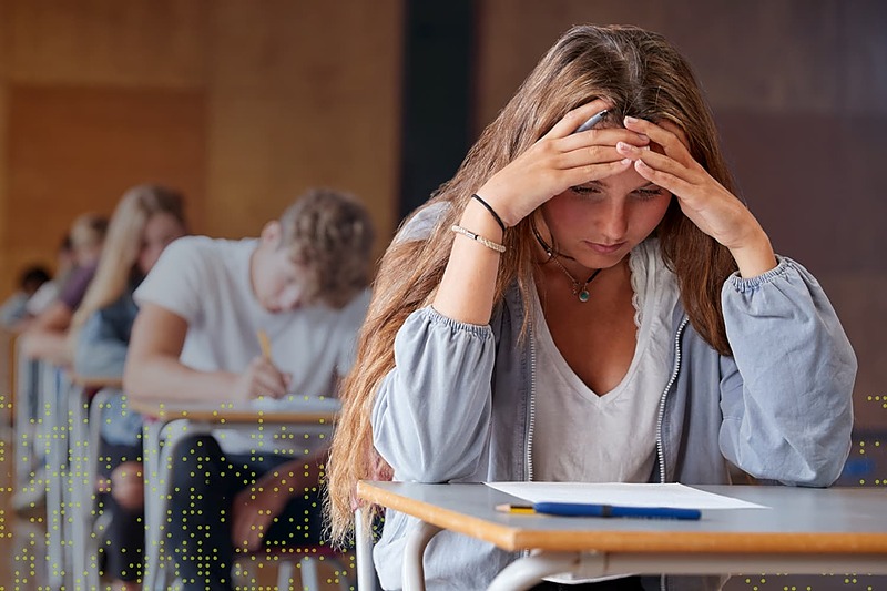 Student sitting at a desk with hands on her head during an exam, showing stress and performance anxiety in a classroom setting.