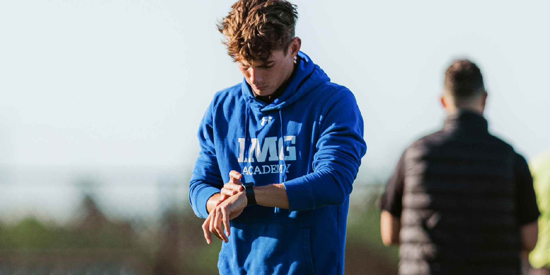 An athlete checks his watch while standing outdoors.