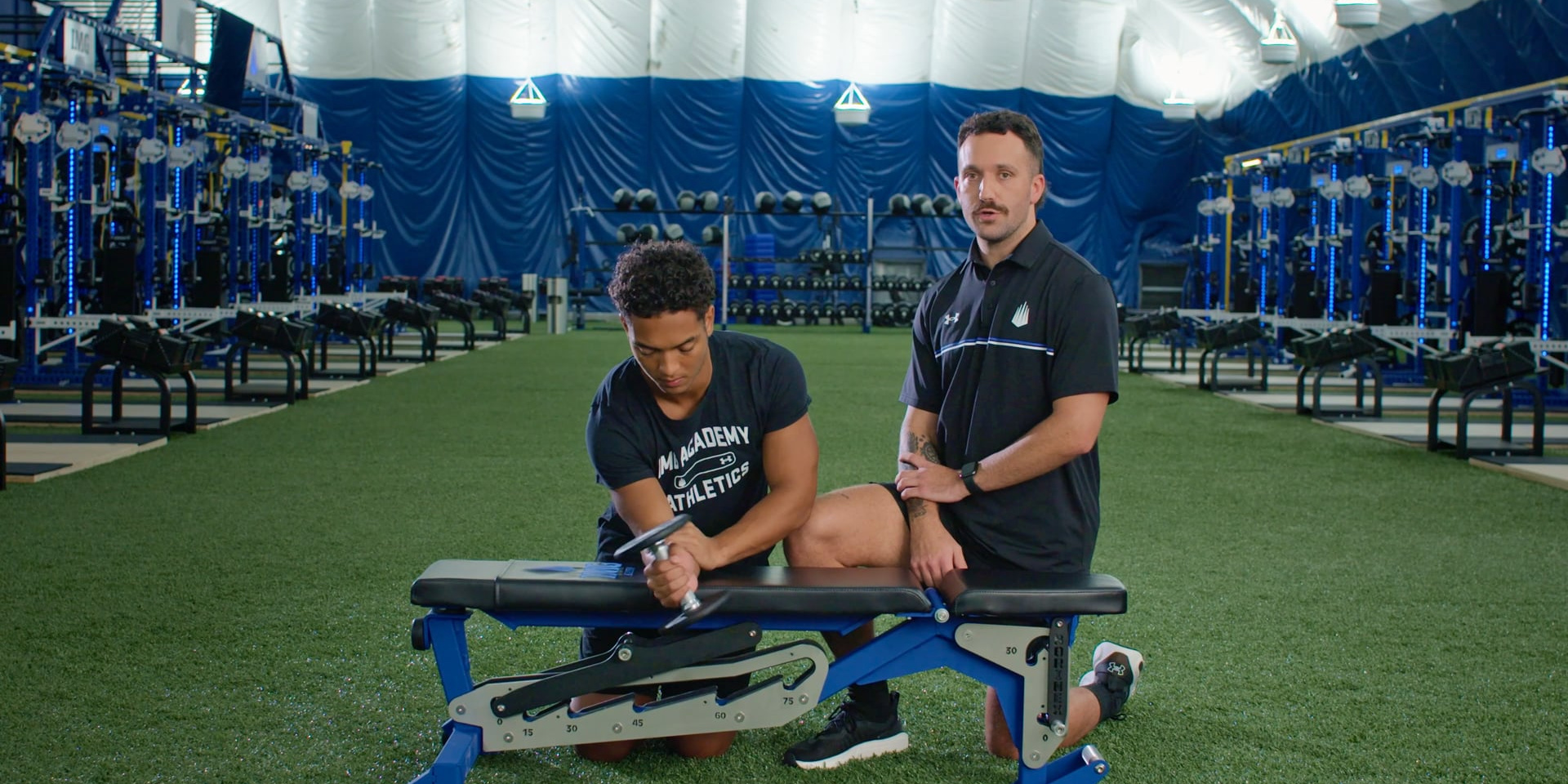 A trainer guides a seated athlete through a forearm exercise using a resistance band.