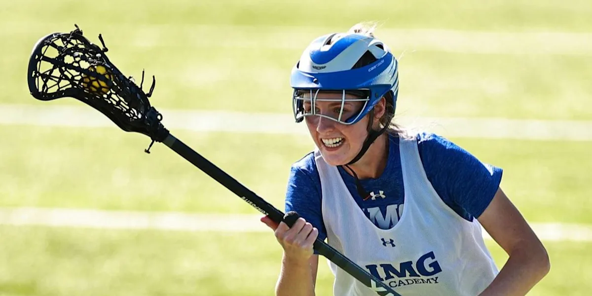 A helmeted lacrosse player runs with his stick and smiles.