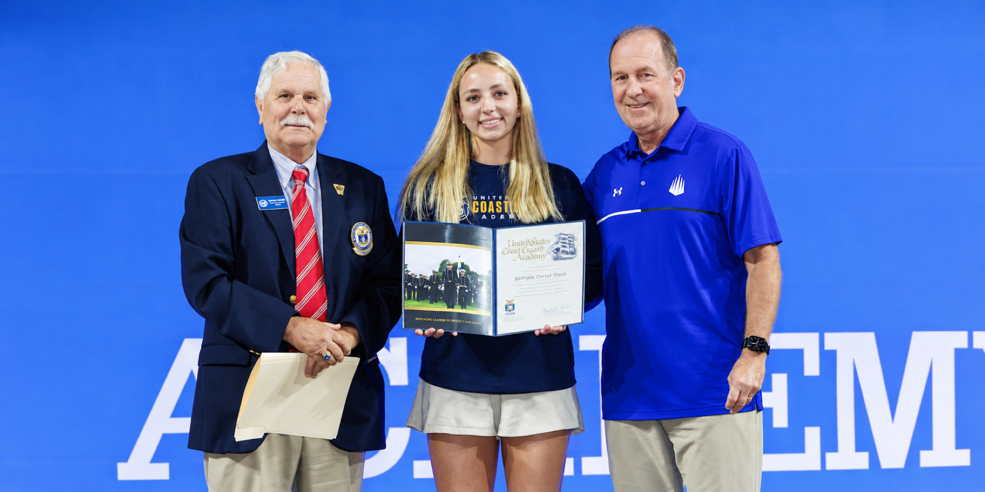 A student-athlete holds a certificate while posing with two adults.