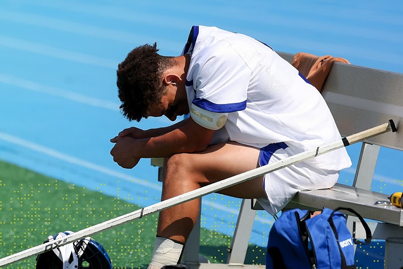 IMG Academy athlete sitting on a bench with head bowed in reflection after a game, representing mental resilience and overcoming mistakes in sport.