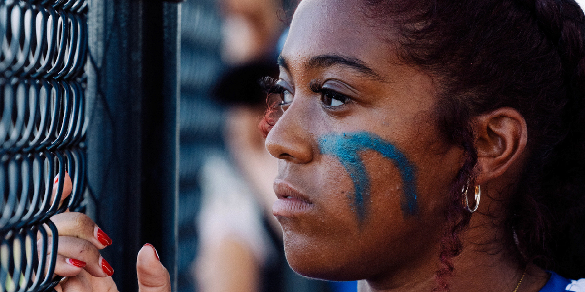 An athlete with face paint looks through a chain-link fence.