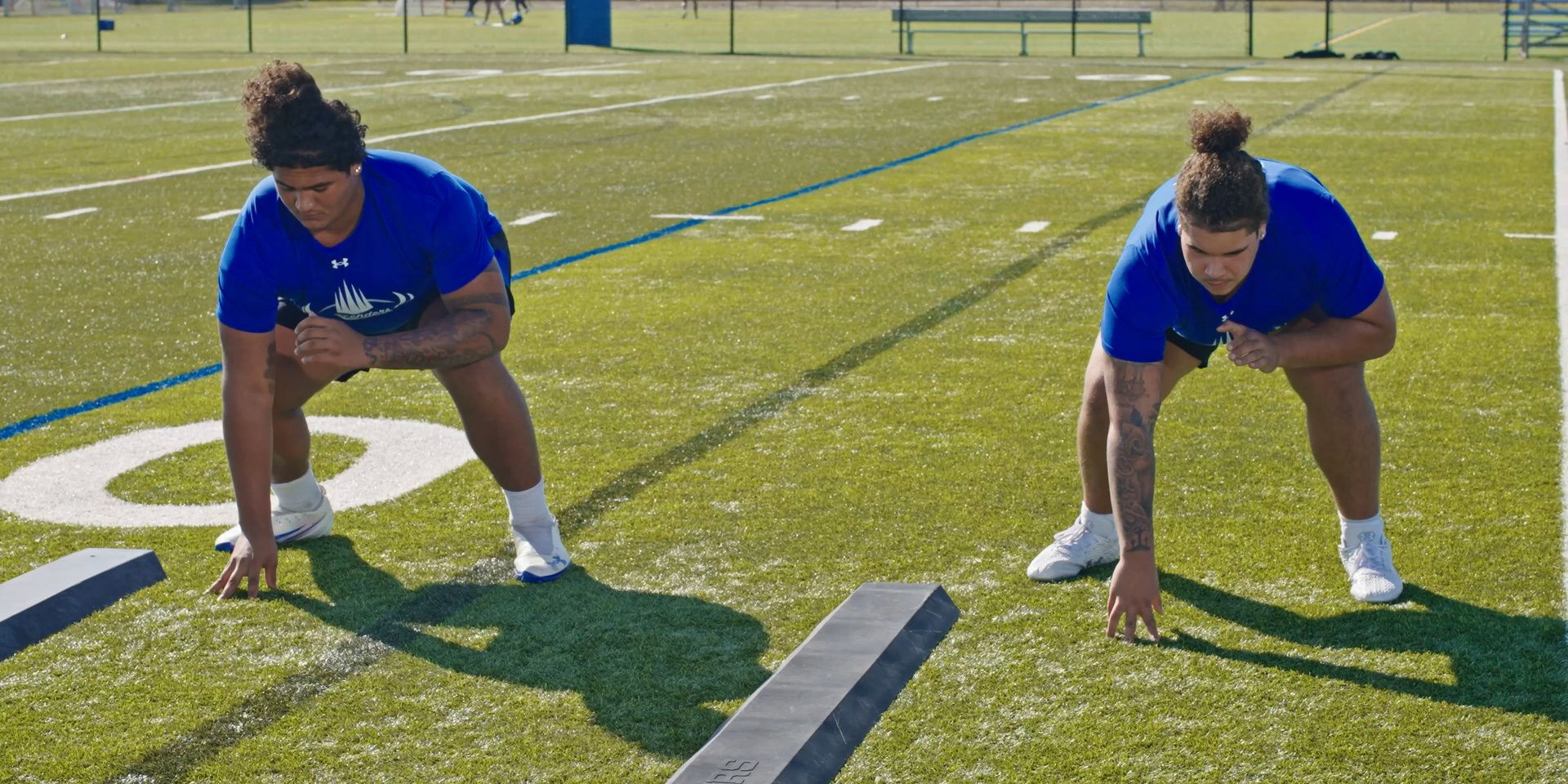 Two football players practice three-point stances on the field.