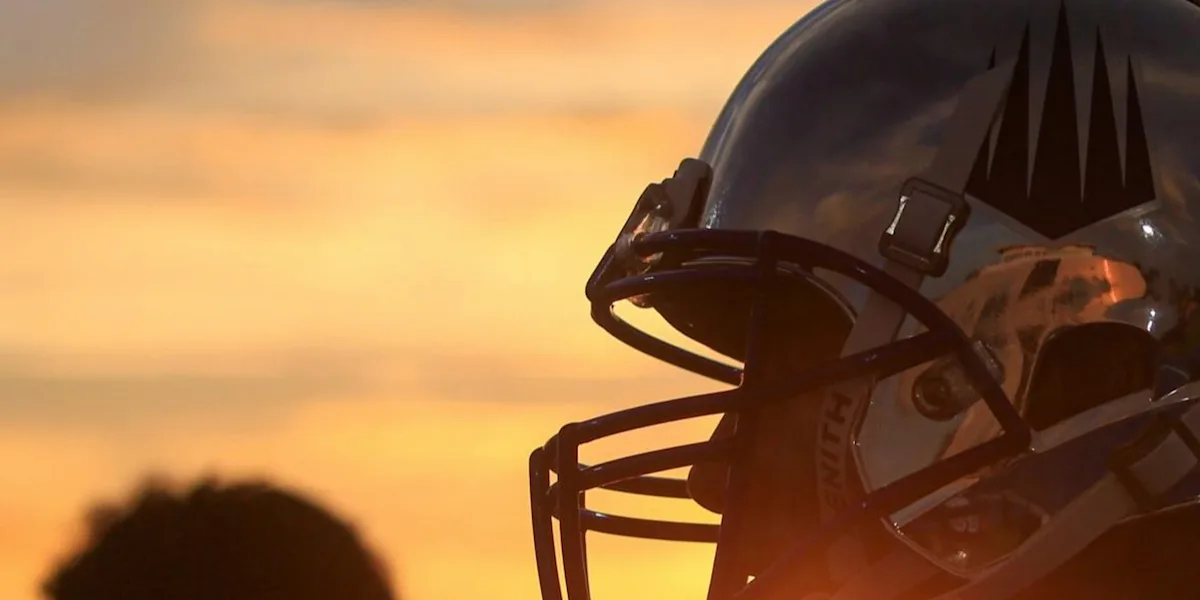 A close view shows a football helmet silhouetted against an orange sunset.