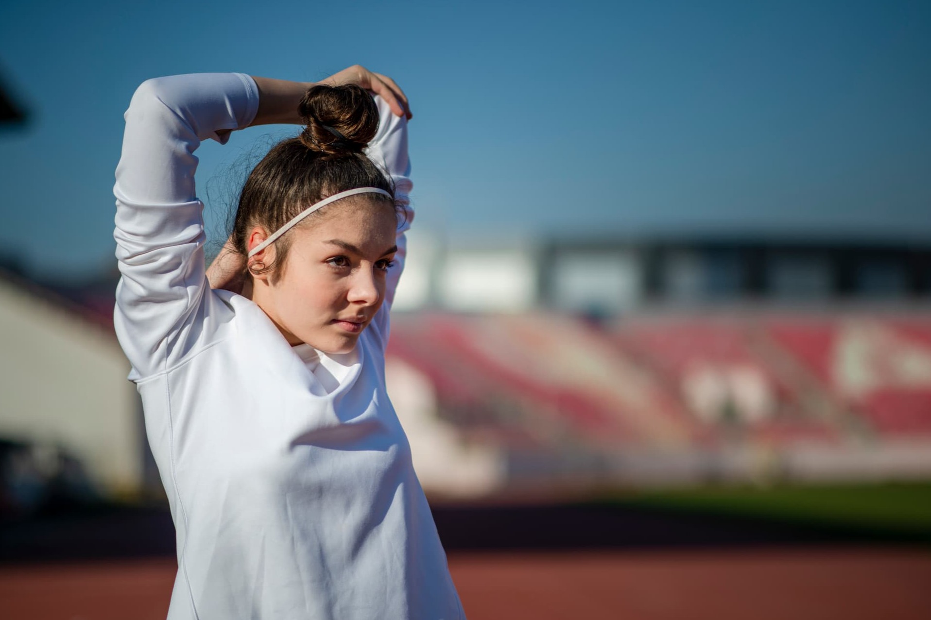 Young athlete warming up with overhead arm stretches outside, in thought and reflection, preparing for training or a competition.