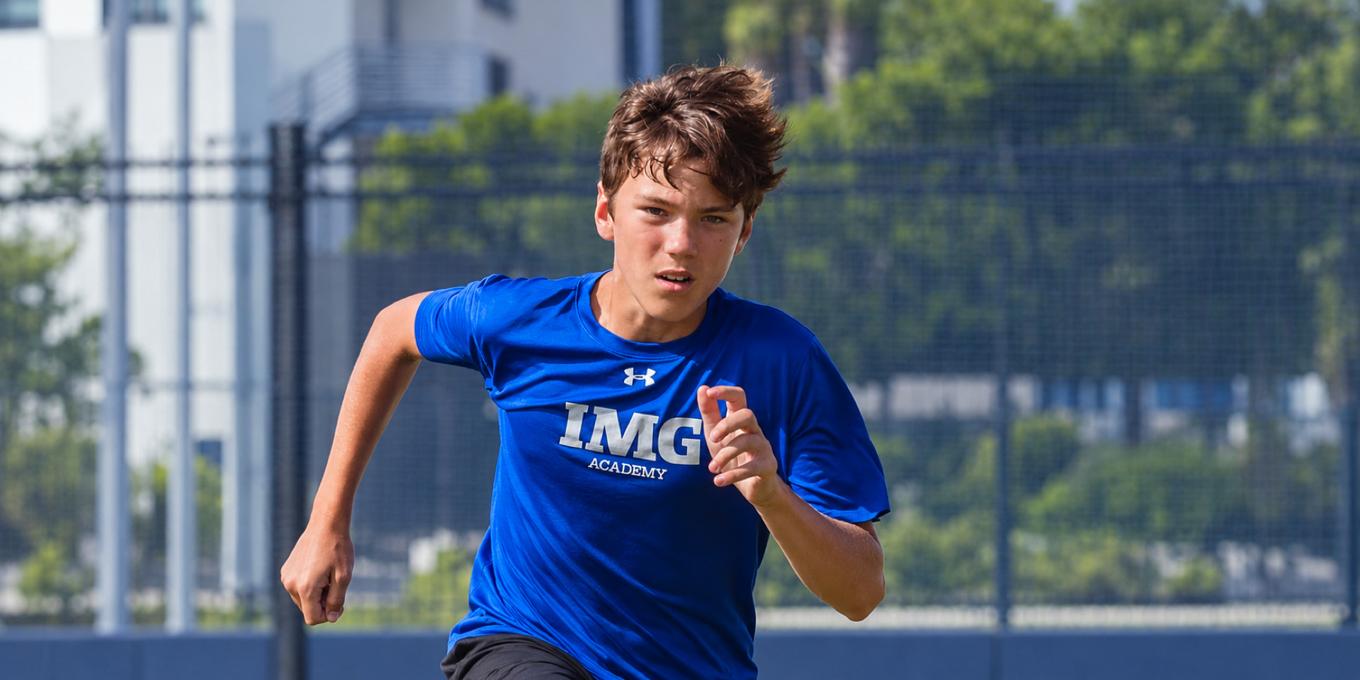 A student-athlete in a blue training shirt runs on an outdoor court.