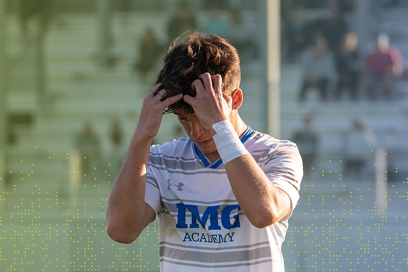 IMG Academy male soccer player standing on the field with hands on his head, reflecting after a moment of frustration during competition.
