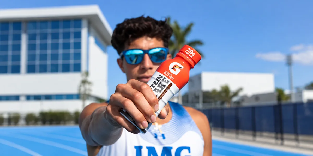 An athlete holds a sports-drink bottle toward the camera.