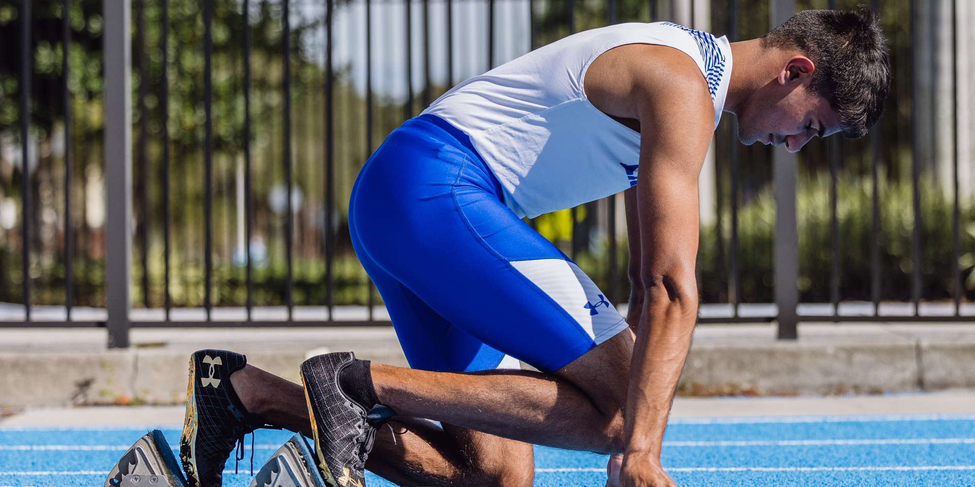 A sprinter kneels at starting blocks on a blue track.