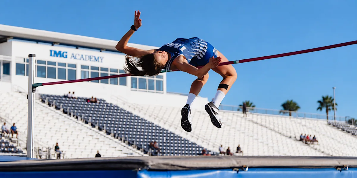 A track athlete clears the high-jump bar at an outdoor stadium.