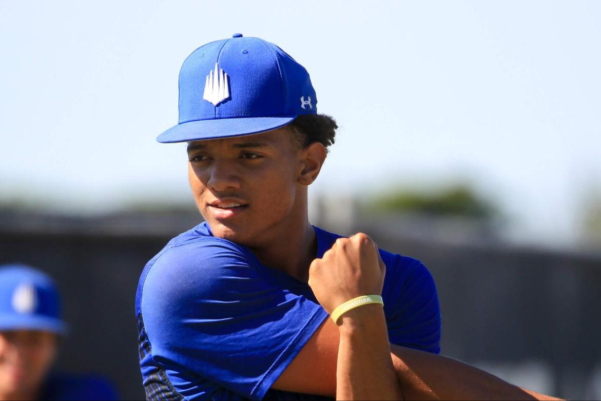 A baseball player in a blue uniform and cap performing a cross-body shoulder stretch during a recovery session.