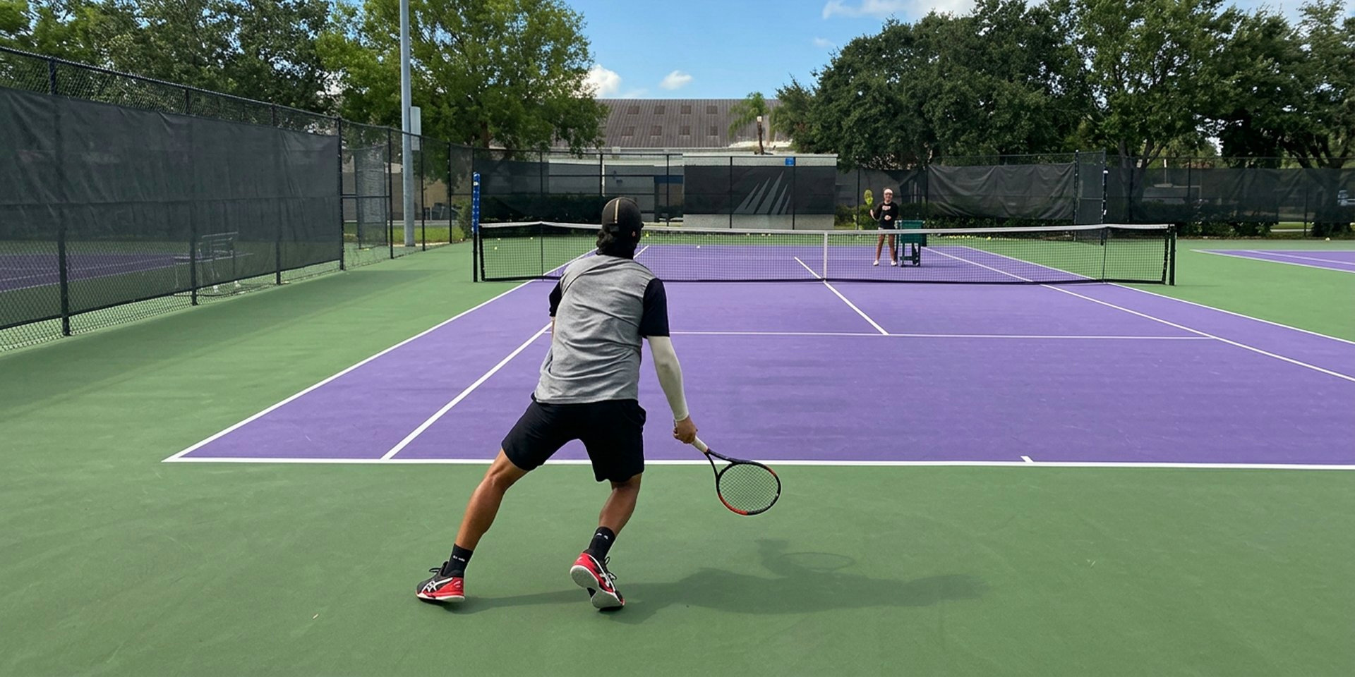 A tennis player waits with a racket on a purple court.