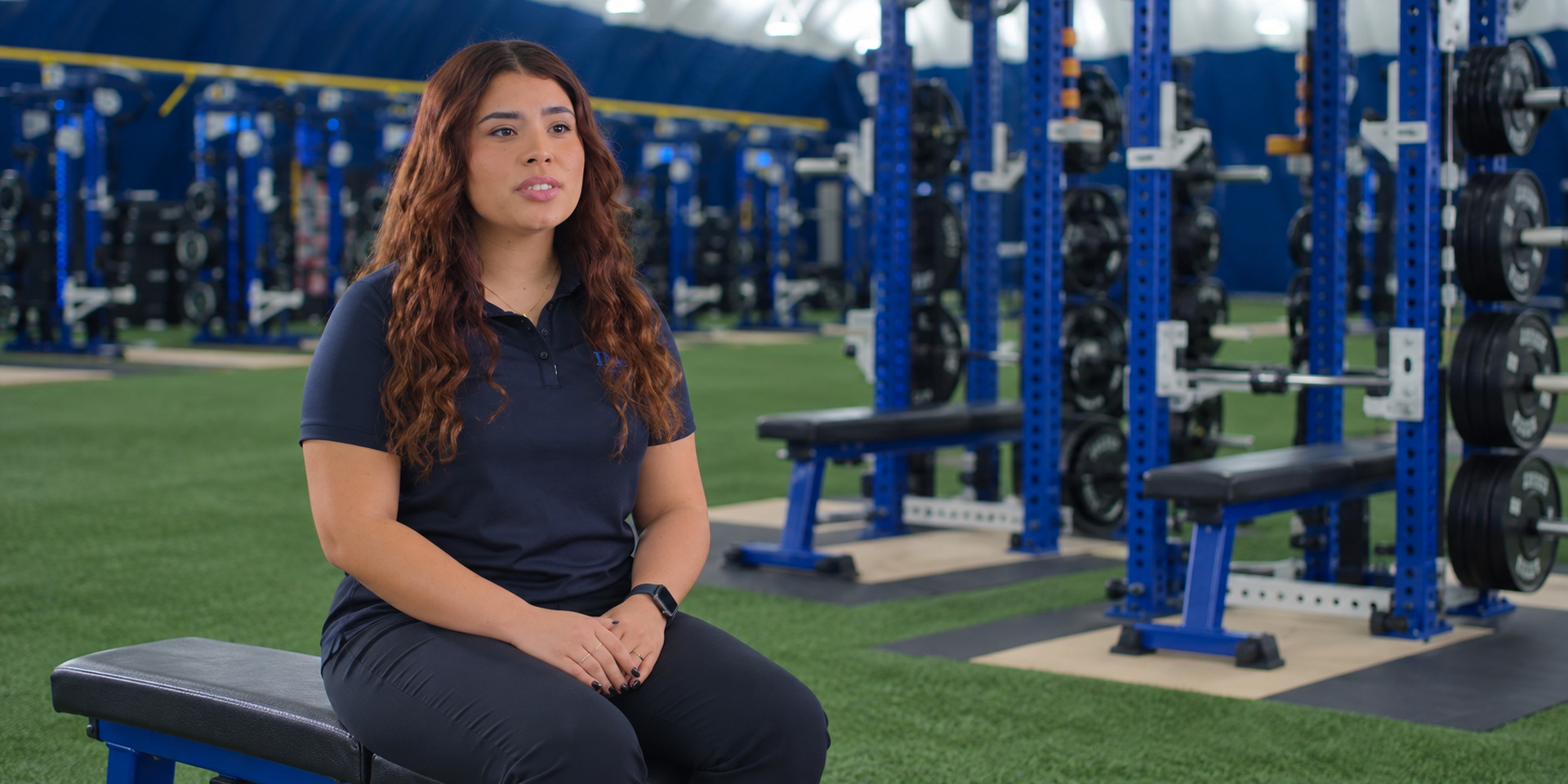 A trainer sits on a bench in the weight room.