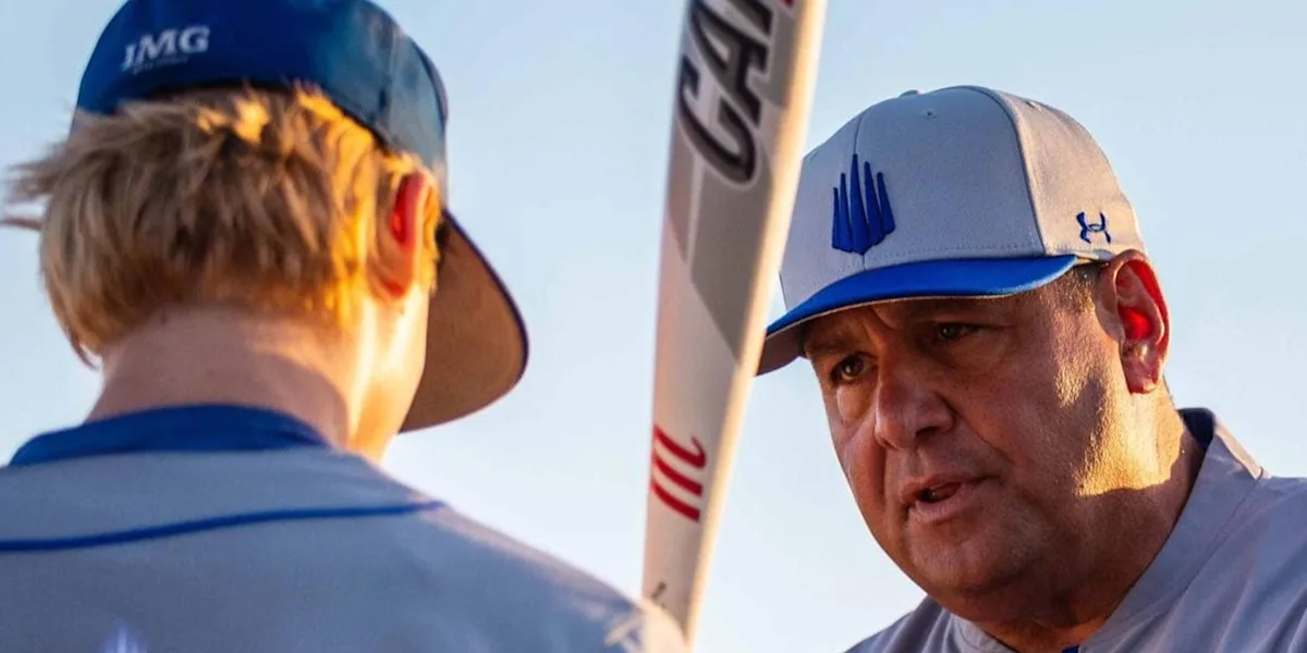 A baseball coach speaks closely with a young player holding a bat.