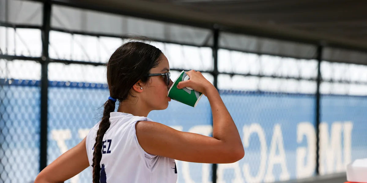 A tennis player drinks from a green bottle beside a court.