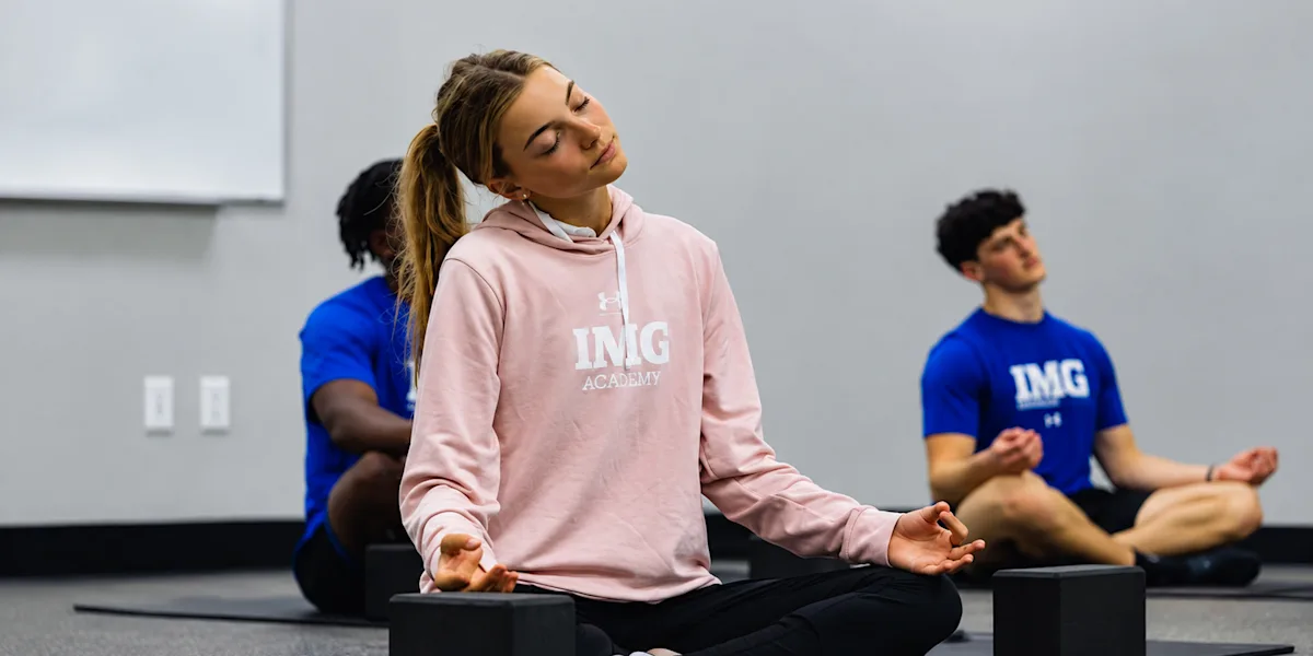 Athletes sit cross-legged on mats during a guided relaxation exercise.