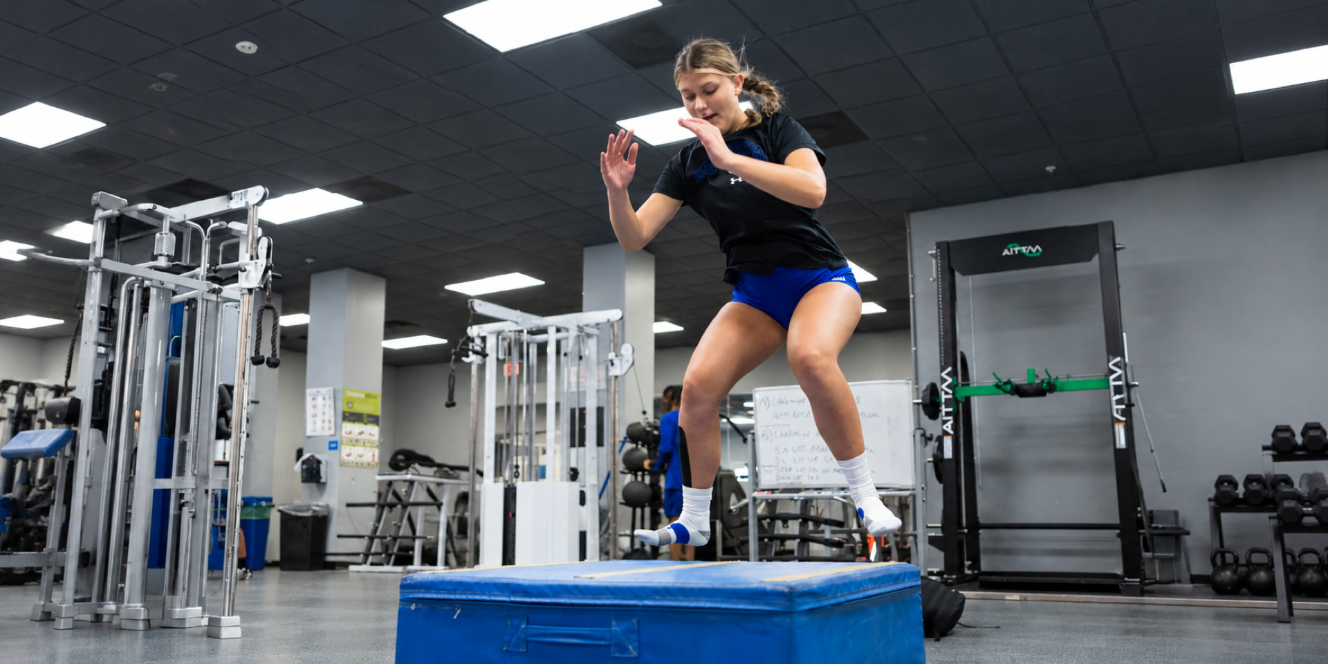 An athlete performs a jump onto a padded box in a gym.