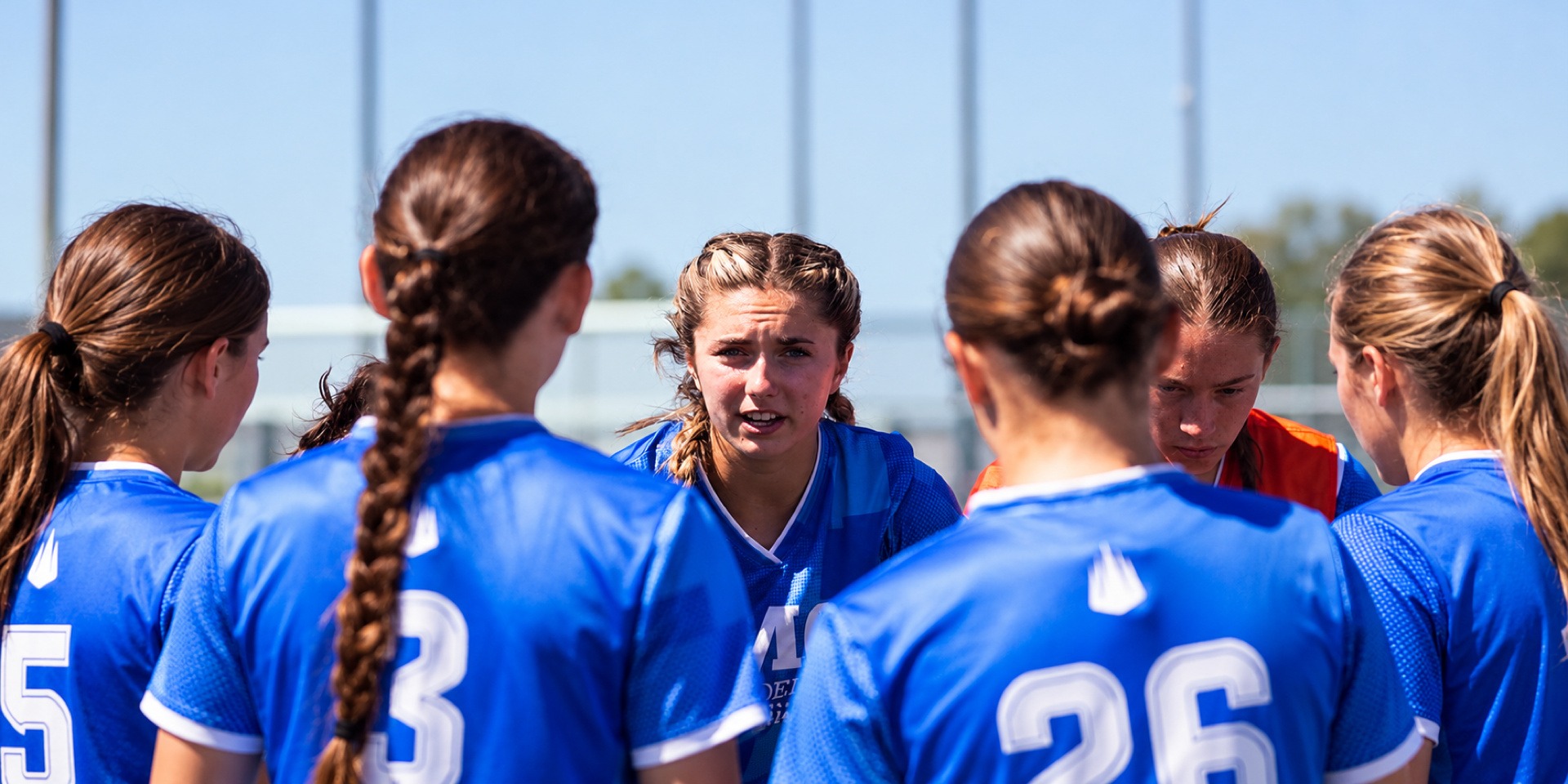 A soccer player speaks to teammates gathered in a huddle on the field.