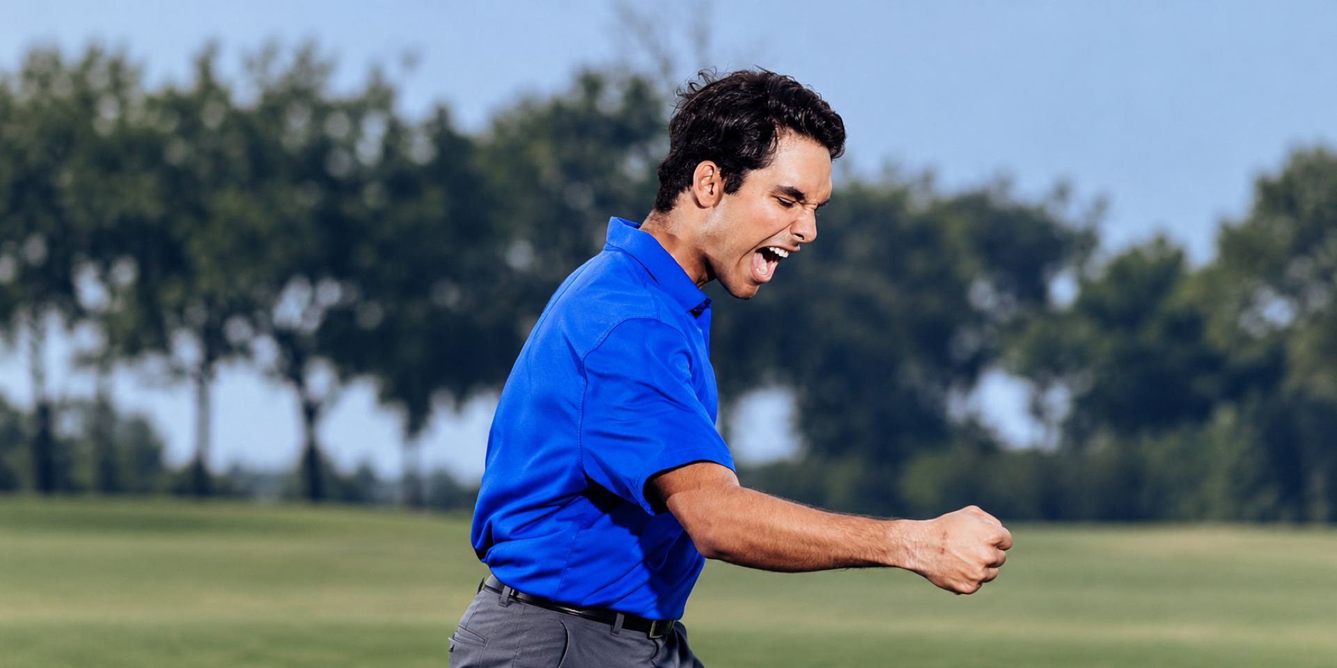 A golfer in a blue shirt celebrates on the course with a clenched fist.