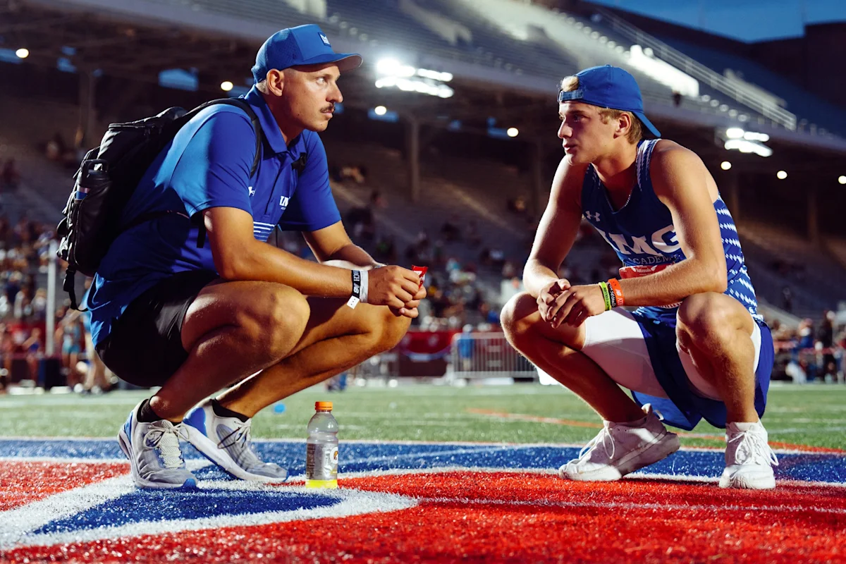 Track and Field coach and athlete reflecting while crouching on a track under stadium lights during Outdoor Nationals.