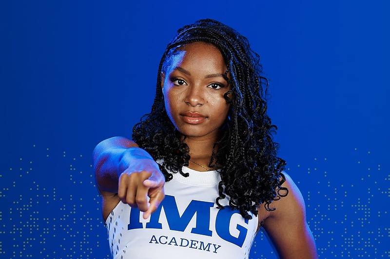 IMG Academy female student-athlete pointing forward against a blue background, conveying confidence, leadership, and personal accountability.