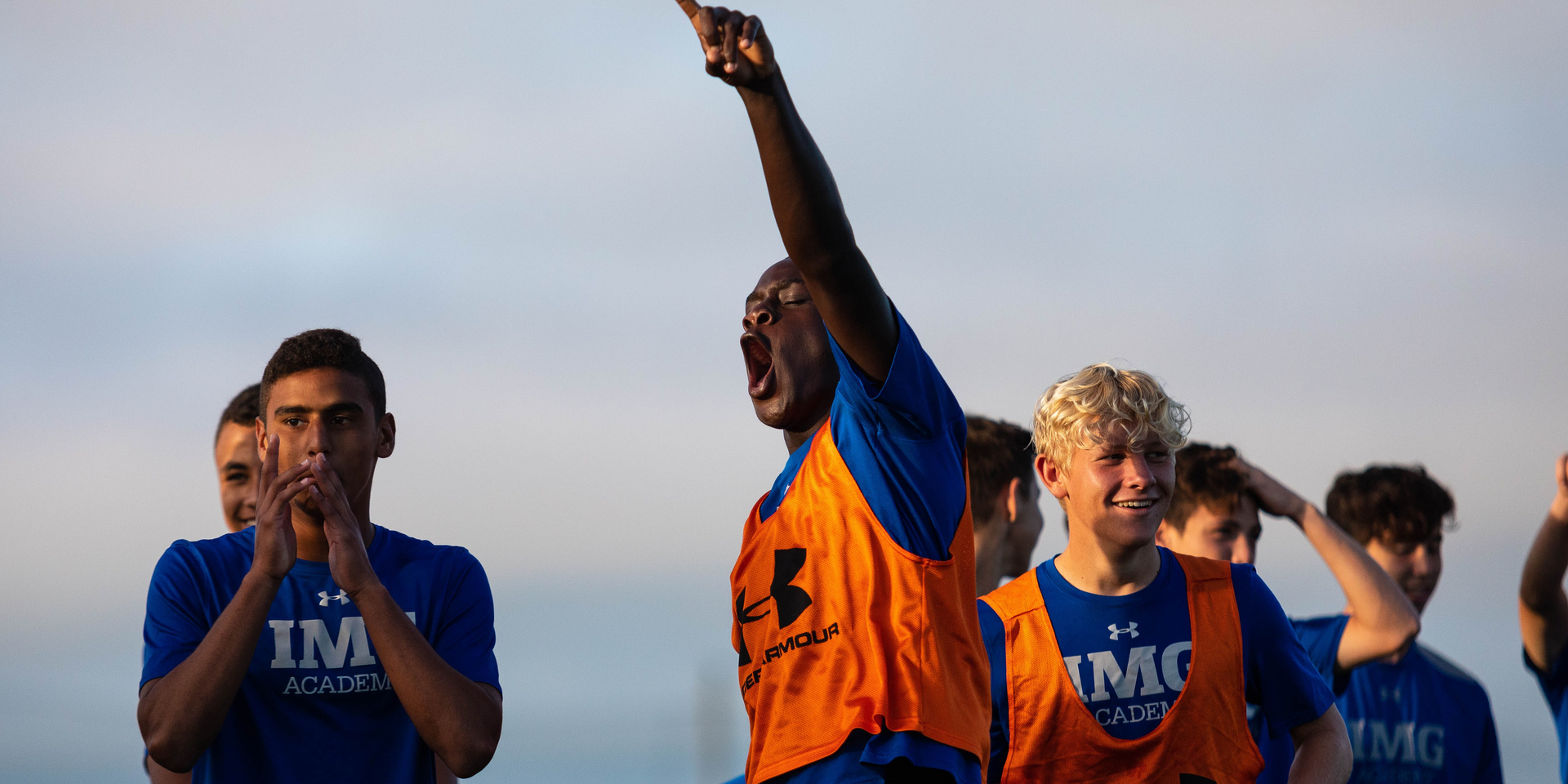 Athletes gather on a field with one raising an arm and pointing upward.