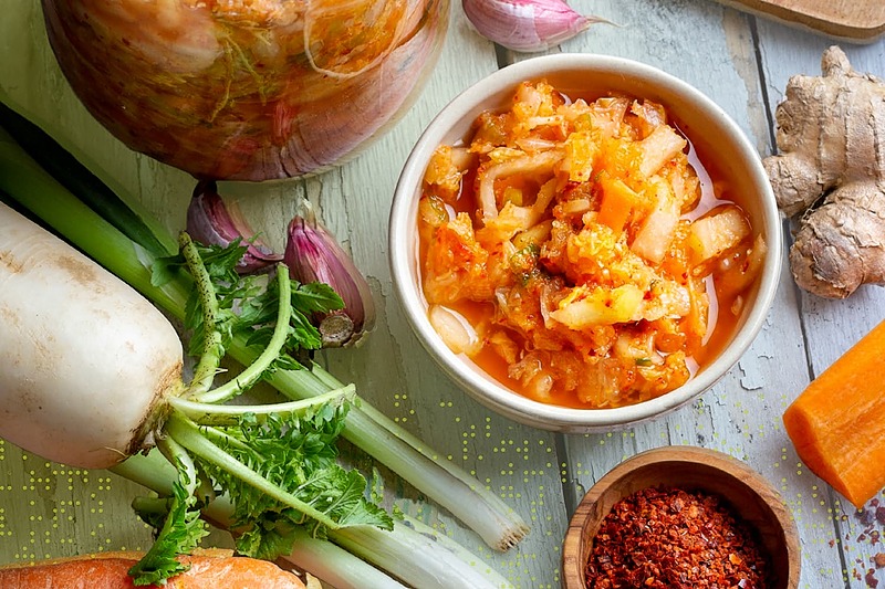 Bowl of fermented vegetables surrounded by fresh produce and spices, illustrating gut-healthy foods.