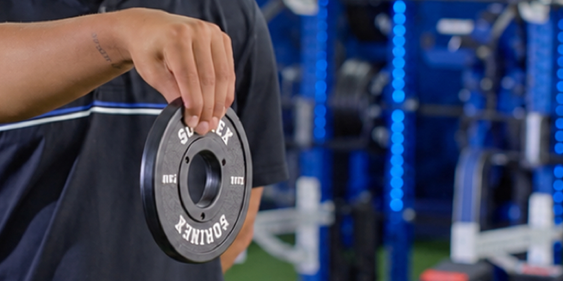 A close view shows an athlete pinching a weight plate with one hand.