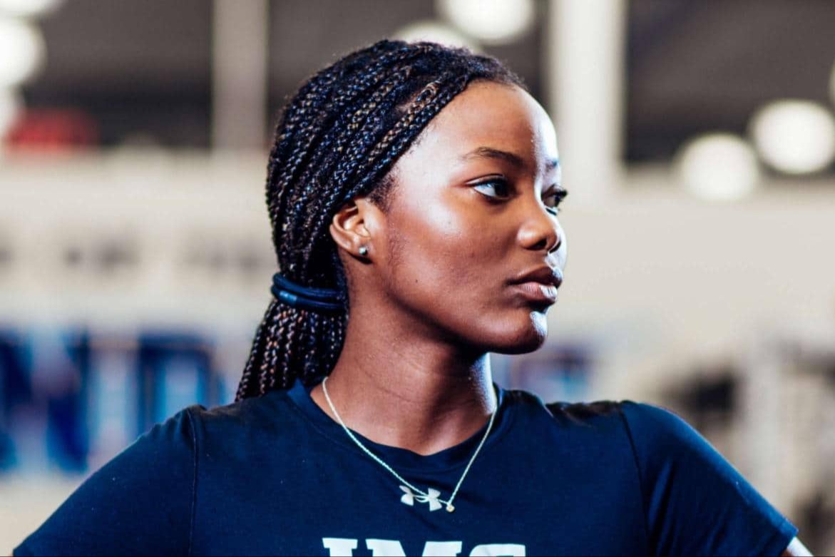 Focused female athlete standing confidently in a training facility, wearing an IMG Academy shirt.