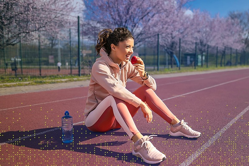 Young IMG Academy athlete sitting on an outdoor track and eating an apple after training, representing healthy fueling, recovery nutrition, and balanced athletic lifestyle.