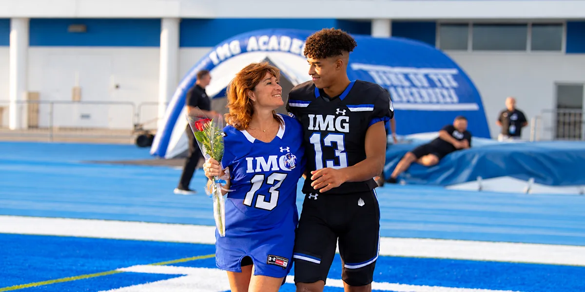 A football player walks arm in arm with a family member beside a track.