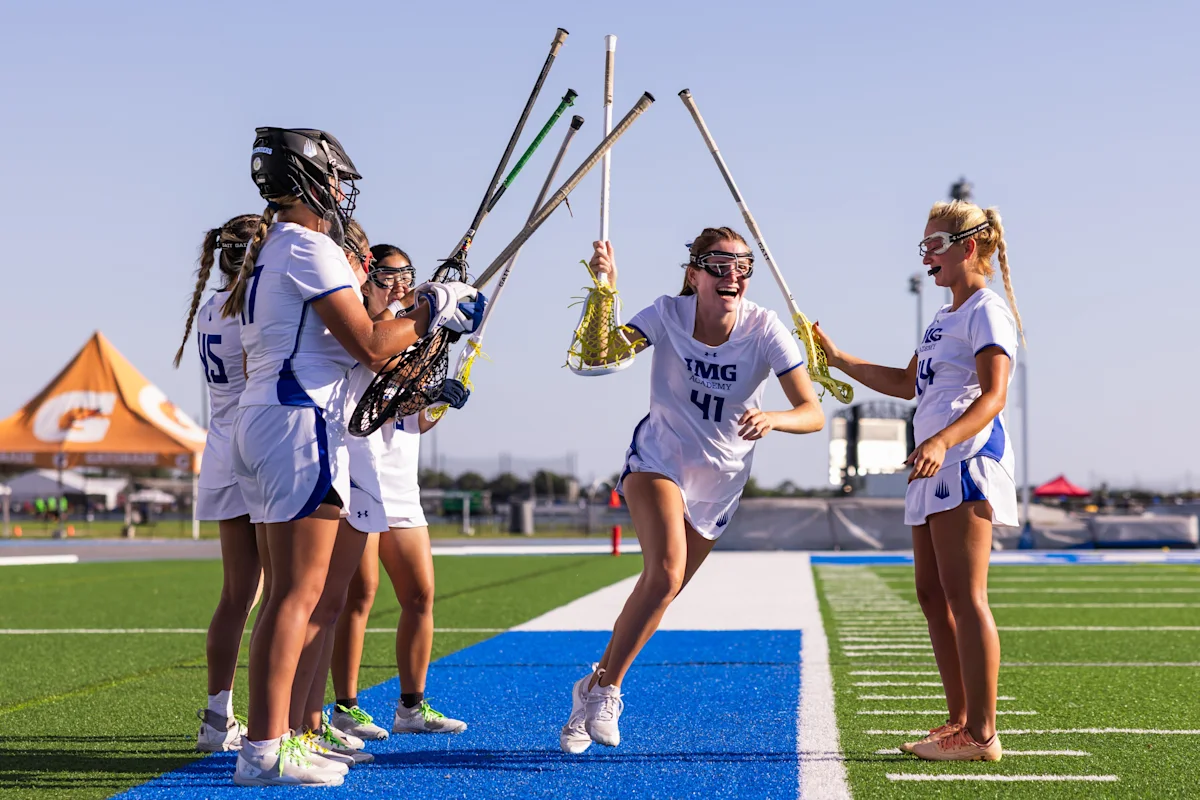 Female lacrosse players celebrating the start of a game on the IMG turf field, illustrating team spirit and athletic excellence in women's sports.