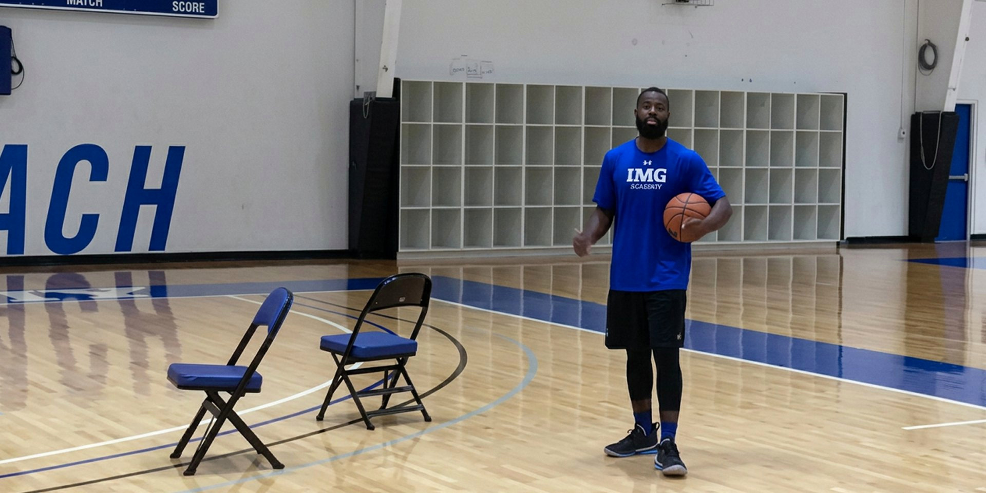 A basketball coach stands beside two chairs holding a ball.