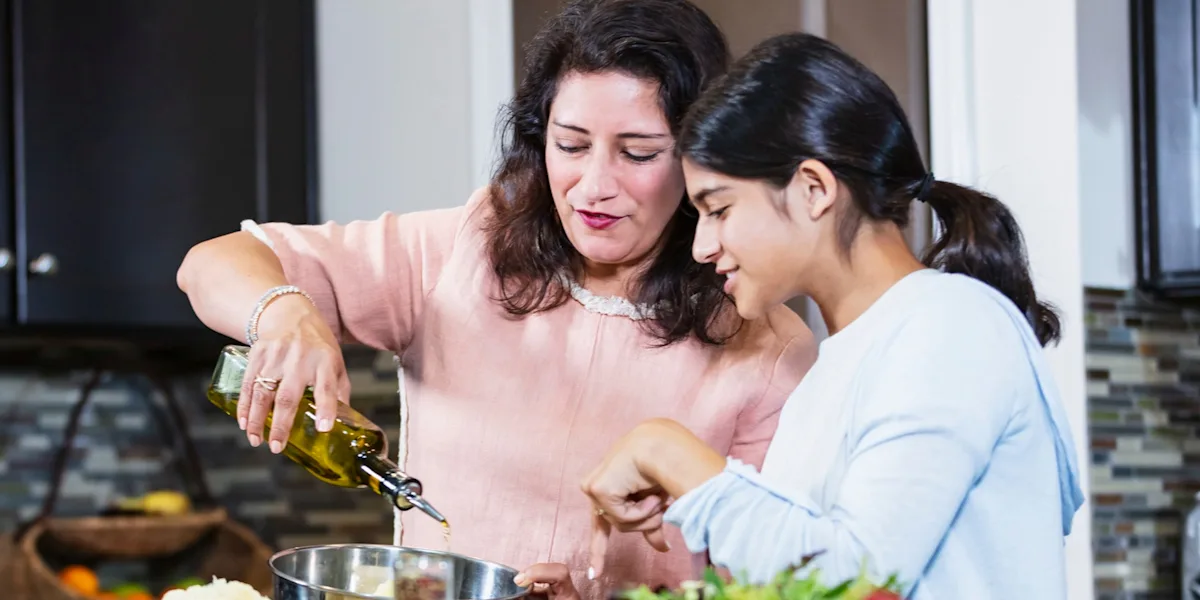 An adult and a student prepare vegetables together in a kitchen.