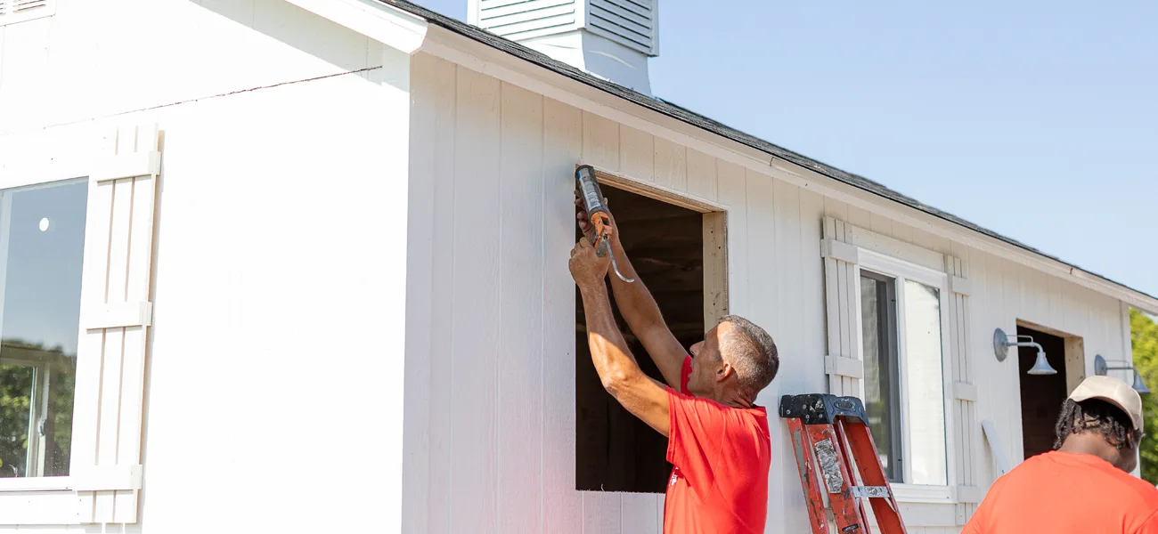 man installing siding on a white shed