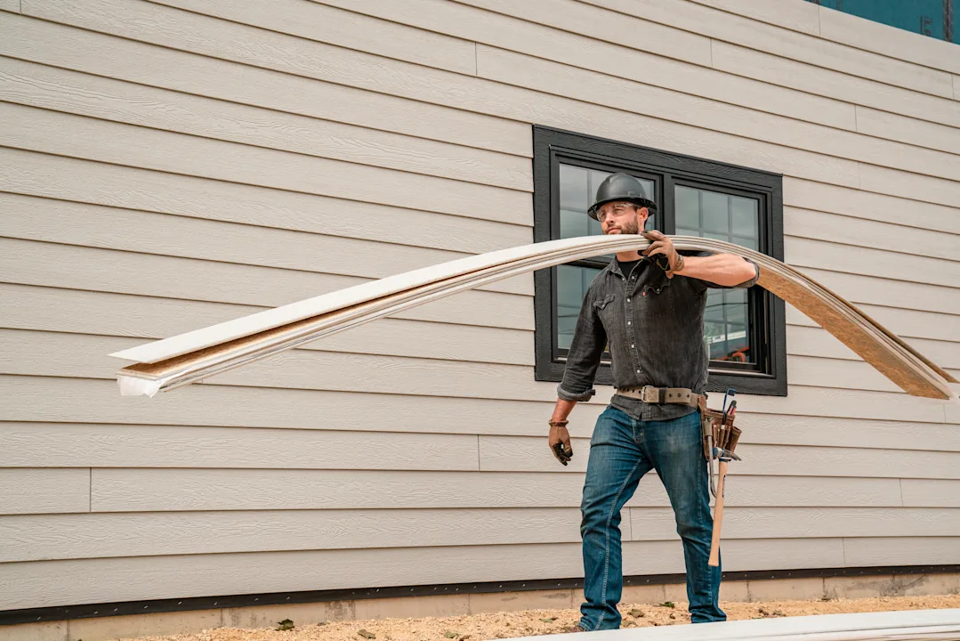 Siding installer carrying siding boards on a jobsite