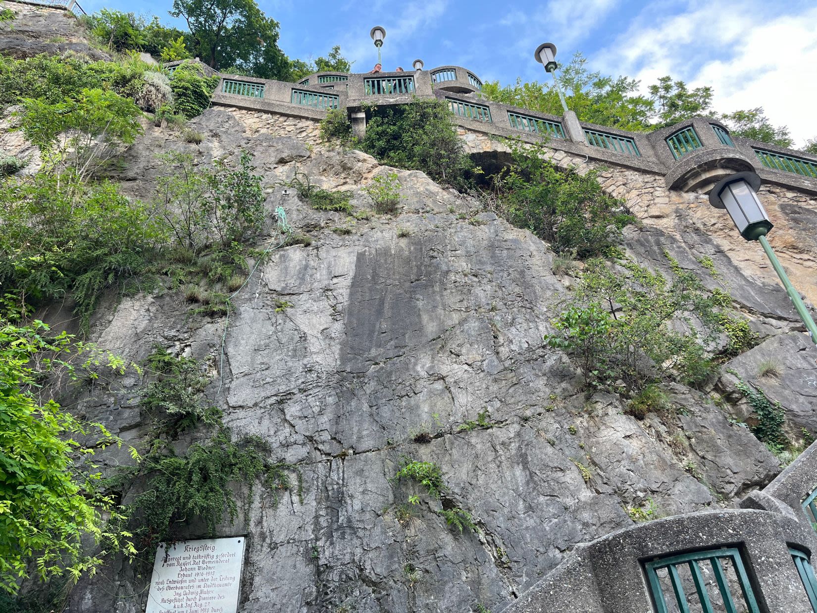 Kamienne schody prowadzące na Schlossberg w Grazu. Ludzie stoją za barierką i patrzą na miasto z góry. 