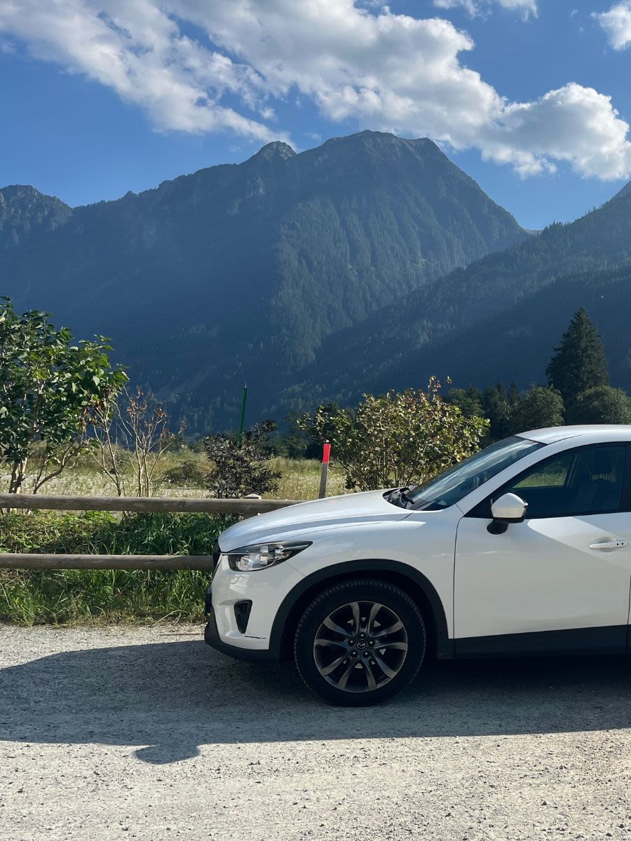 Biały samochód marki Mazda CX-5 stoi zaparkowany w pobliżu jeziora Lago di Poschiavo w Szwajcarii.