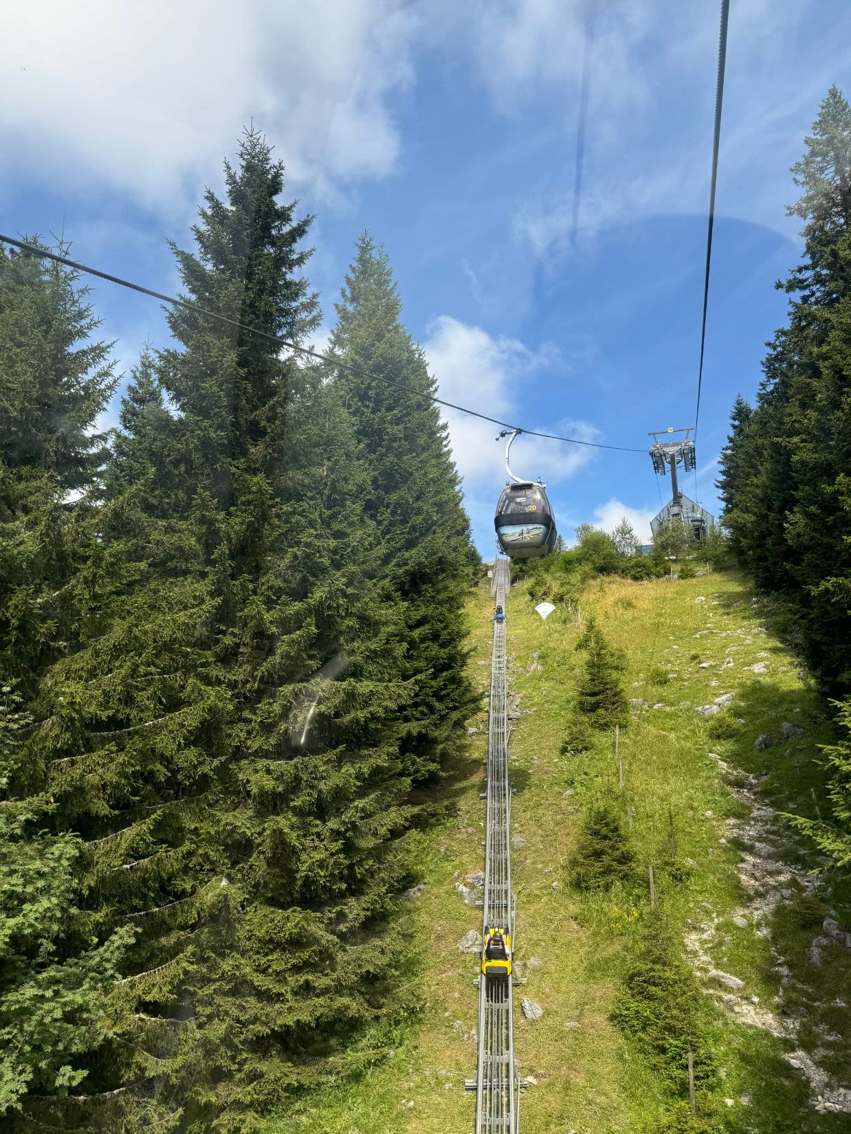 Wagon kolejki linowej zjeżdża z góry Schöckl w Austrii. Pod nimi na ziemi zamontowany jest tor saneczkowy Hexenexpress - Sommerrodelbahn, po którym zjeżdżają sanki.