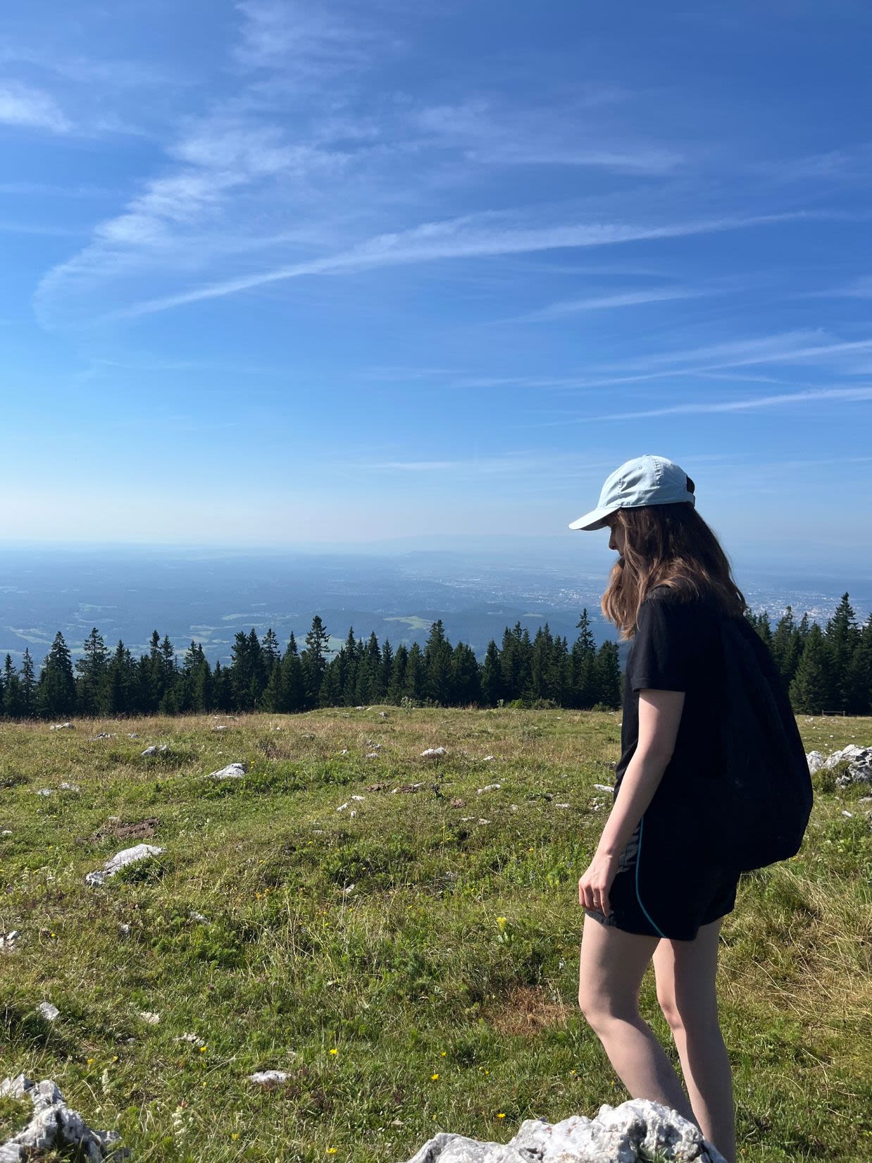 Autorka bloga Słowa Płyną na szczycie Schöckl. Na polanie znajdują się większe kamienie. Dalej ściana lasu, a dalej szeroka panorama Styrii. 