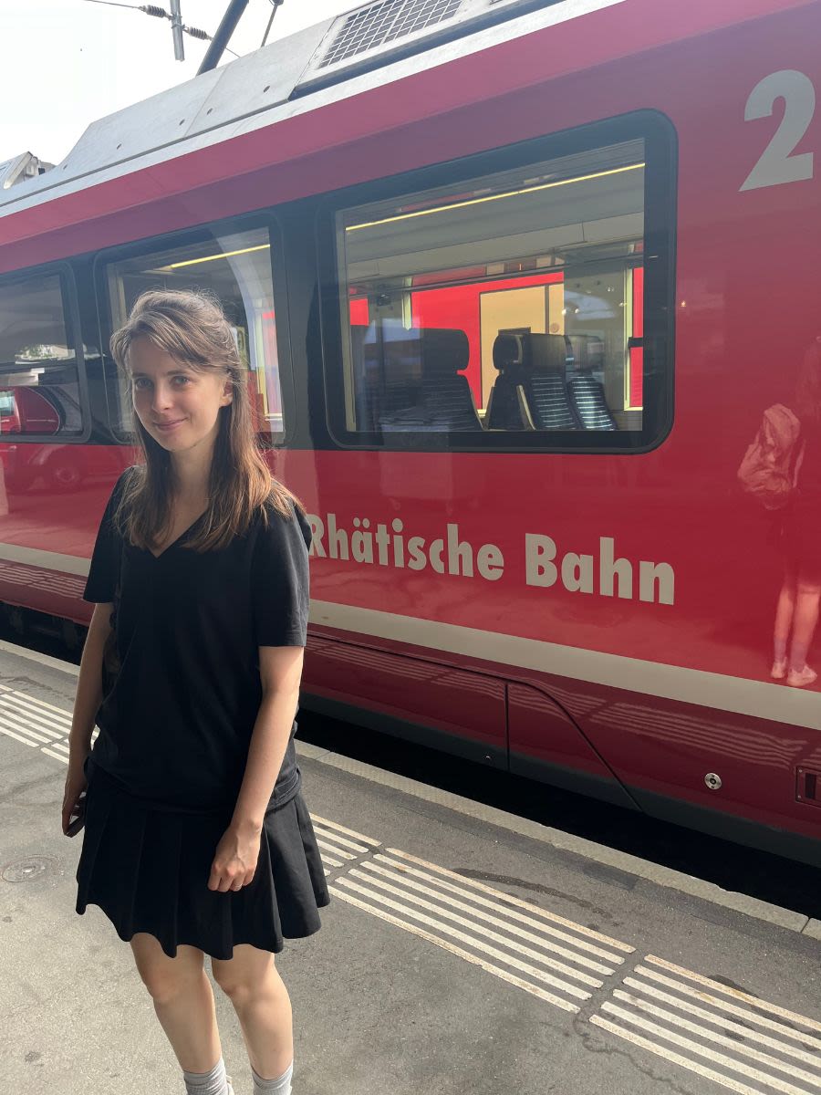 Autorka bloga Słowa Płyną Paulina Klaman stoi przed czerwonym pociągiem na stacji Davos w Szwajcarii.