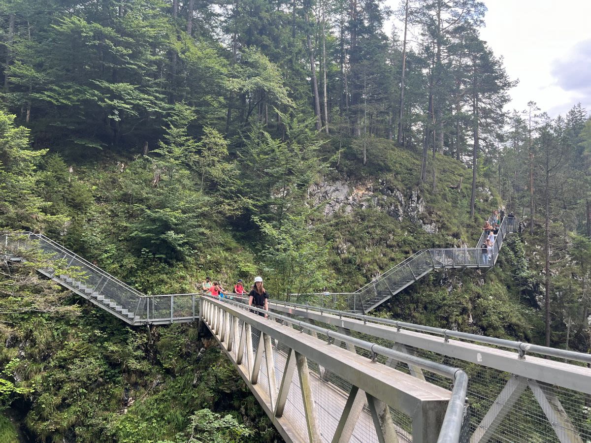 Autorka bloga Słowa Płyną Paulina Klaman stoi na panoramicznym moście Panorama-Brücke w wąwozie Leutascher Geisterklamm. Za mostem znajdują się metalowi kładki.