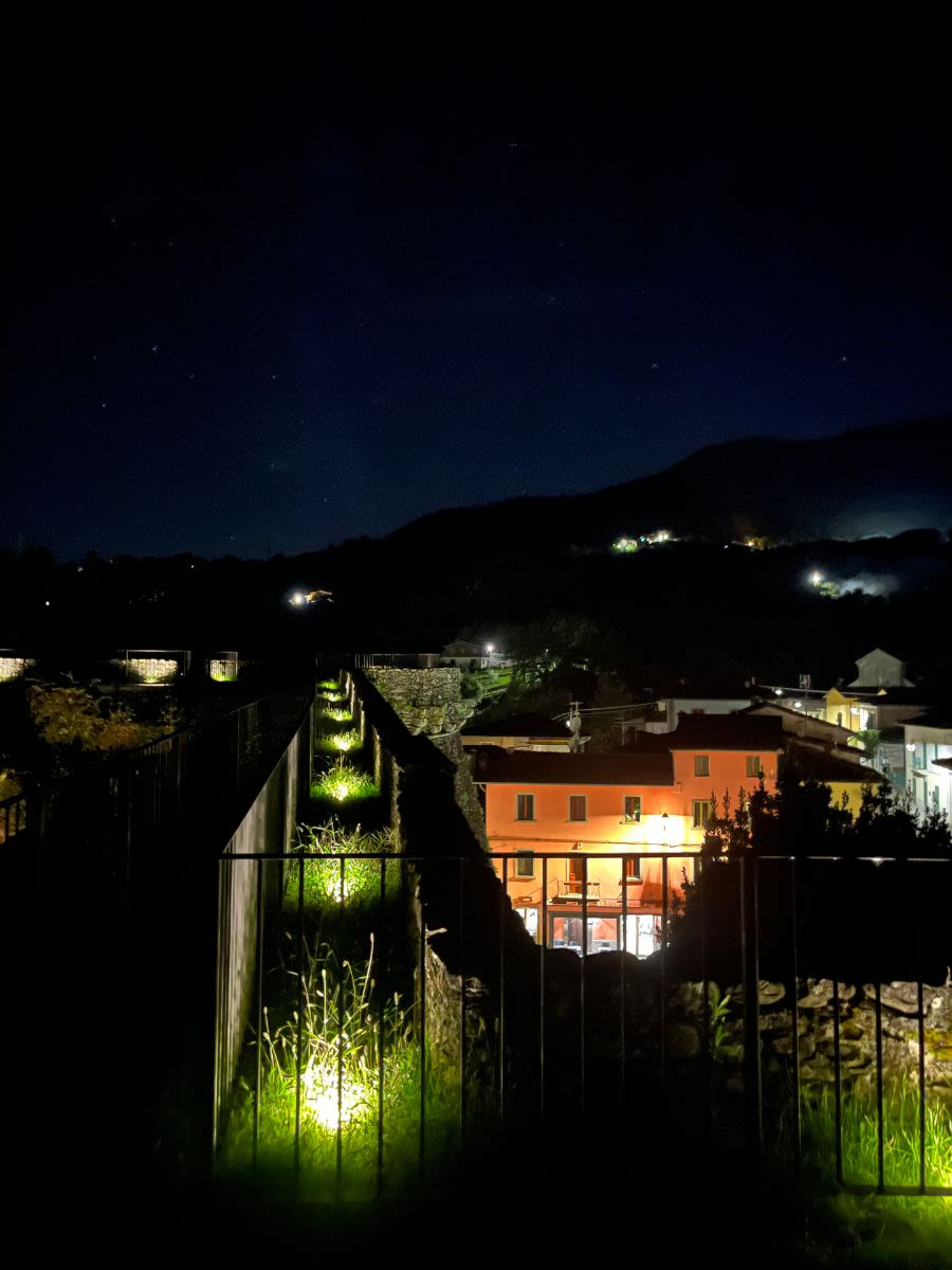 Widok z fortu La Rocca di Camporgiano na miasteczko. Domy są oświetlone. Niebo jest czyste, pokryte gwiazdami.
