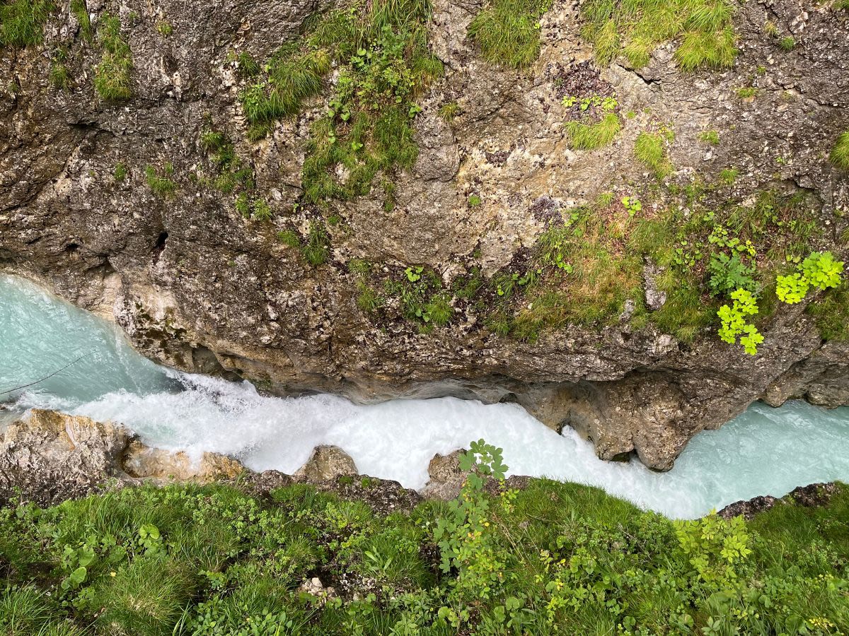 Wąwóz Leutascher Geisterklamm, w dole rwąca rzeka Leutascher Ache. Woda w rzece jest niebieska, w niektórych miejscach się pieni. Zbocza wąwozu porasta niska roślinność.