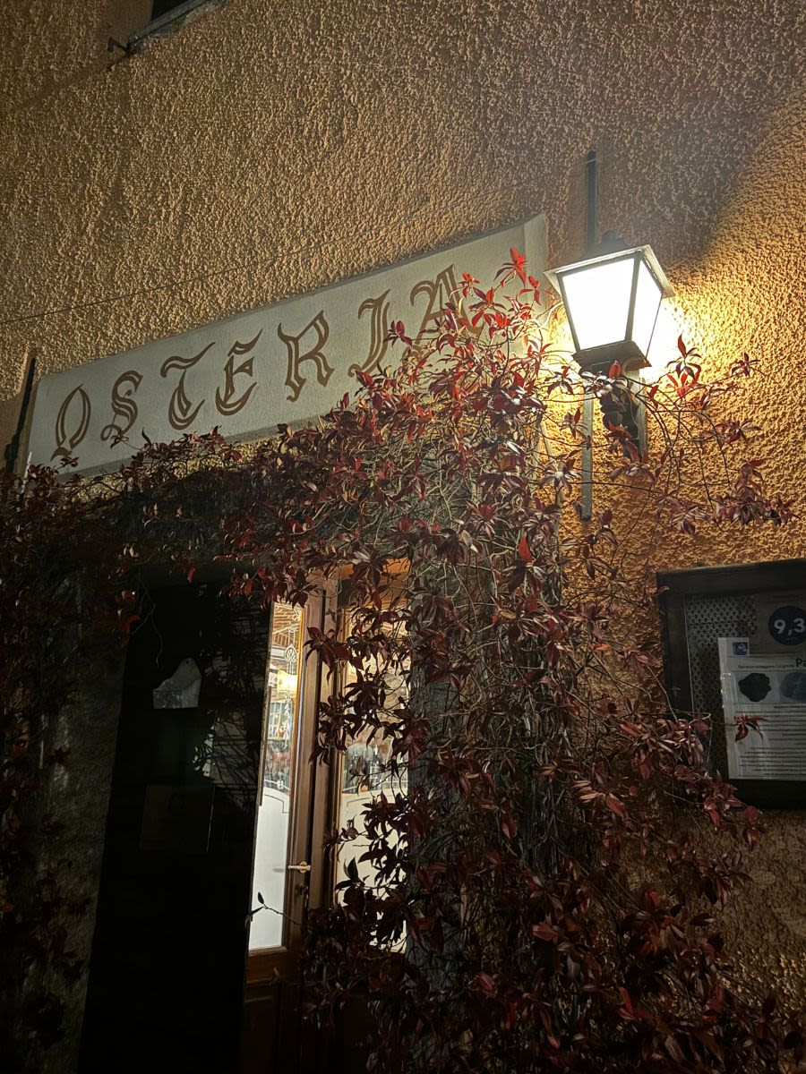 Drzwi wejściowe do restauracji Osteria Vecchia Capronno. Jest wieczór, nad drzwiami świeci się lampa.